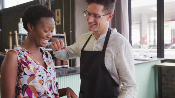 Portrait of happy diverse couple working at a cafe bar, standing by the bar and smiling to camera