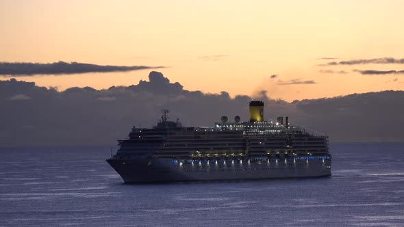 Cruise ship sailing at sea during sunset, warm orange and red color.