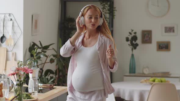 Happy Pregnant Woman in Headphones Dancing at Home