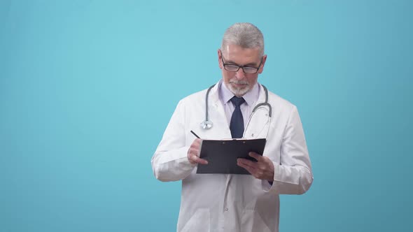 Adult man doctor in a medical uniform and glasses writes with a pen on paper tablet and smiles