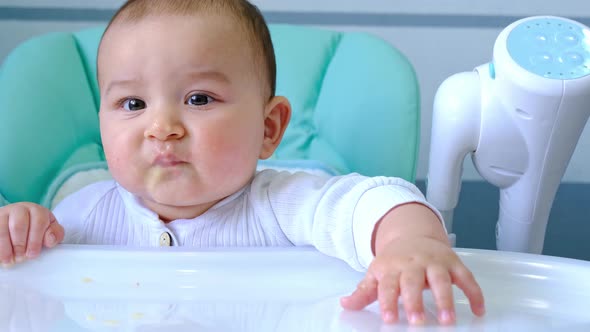 A hungry baby taps his hand on the table on a high chair, asks to eat, nibbles on a spoon. Teething,