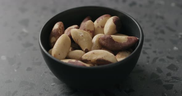 Slow Motion Man Hand Takes Brazil Nuts From Black Bowl on Terrazzo Countertop