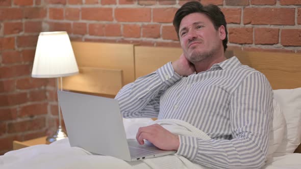 Middle Aged Man with Neck Pain working on Laptop in Bed