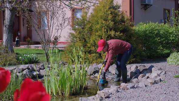 Woman Lets Down a Submersible Water Pump Into an Artificial Garden Pond