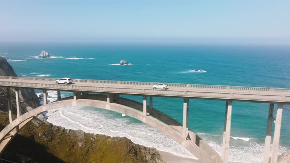 Cars Driving Slow By Scenic Arch Architecture Bridge with Blue Ocean Background