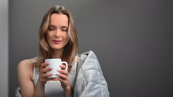 Female with Fresh Skin Drinking Coffee Wrapped in Blanket