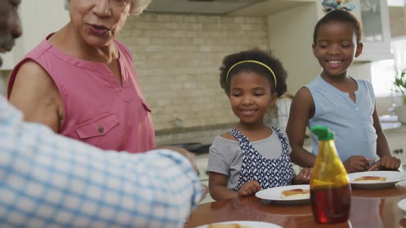 Happy african american grandparents with granddaughters having breakfast and talking