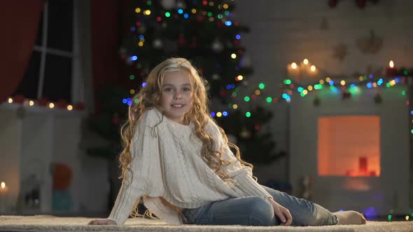 Little Adorable Girl on Floor Under Decorated X-Mas Tree, Smiling to Camera