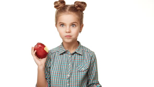Small Cute Caucasian Caucasian Kid Girl with Plaid Shirt and Two Hair Buns Eating Red Apple with