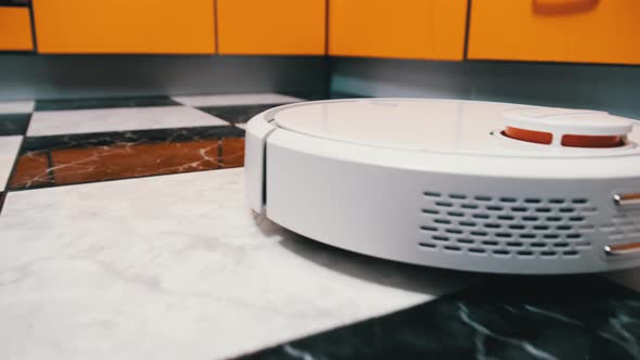 The Robot Vacuum Cleaner Cleans in the Modern House on the Tiles Floor at Kitchen