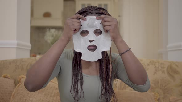 Portrait of Pretty African American Woman Putting Moisturizing Facial Mask on Her Face on the Coach