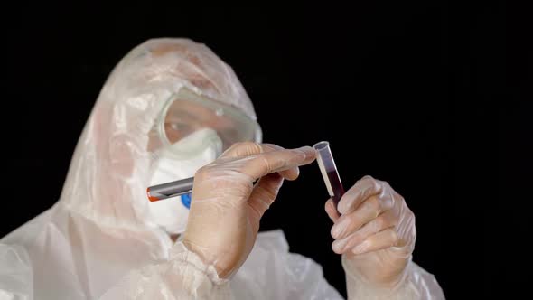 Virologist in Protective Costume Respirator Mask and Gloves Analyzing Tube with Blood