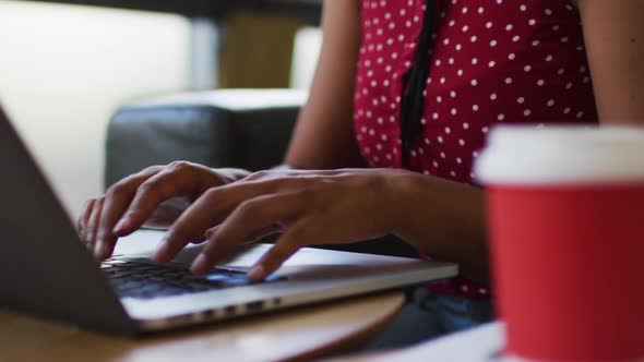 Mixed race woman going through paperwork drinking coffee using laptop in the office