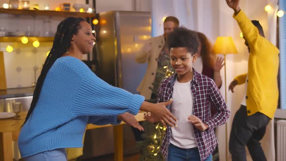 Young African Woman Dancing with Son While Friends Having Fun on Background Celebrating New Year