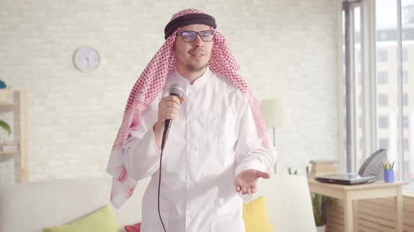 Cheerful Arab Man in Traditional Clothes Singing in Karaoke Microphone at Home