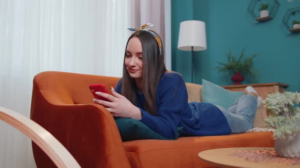 Young Caucasian Woman Lying on Couch Using Smartphone Watching Video Online Shopping Tapping