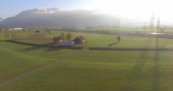 Paning from a green field to a house with a farm, the chimney is smoking.