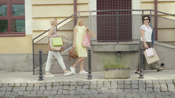 Side View of Confident Caucasian Mid-adult Shoppers Strolling on City Street on Black Friday. Wide