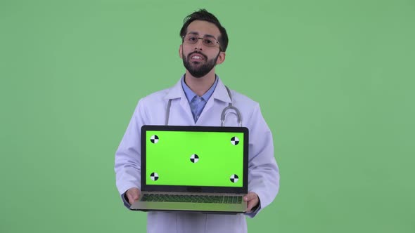 Happy Young Bearded Persian Man Doctor Talking While Showing Laptop