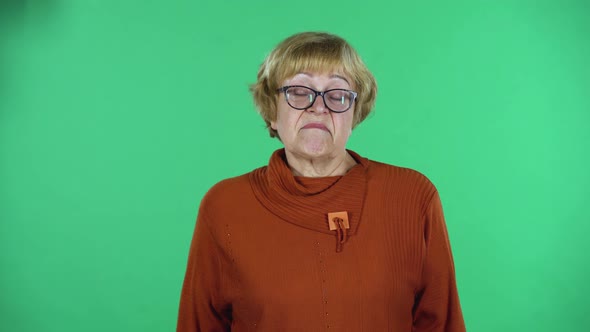 Portrait of Senior Woman Is Looking Straight and Shrugging Isolated Over Green Background.