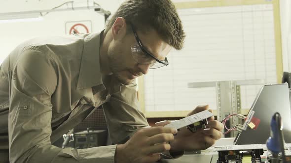 Electrical engineer scrutinizing circuit board and then smiling at camera