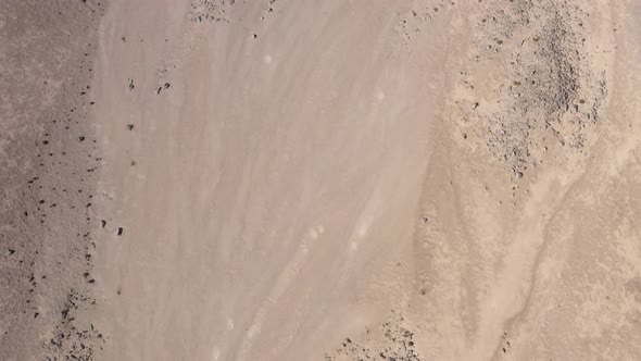 Flying over a barren landscape of brown grey sand and rock formations with many craters