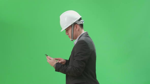 Side View Of Asian Chief Engineer In The Hard Hat Use Mobile Phone While Walking On Green Screen