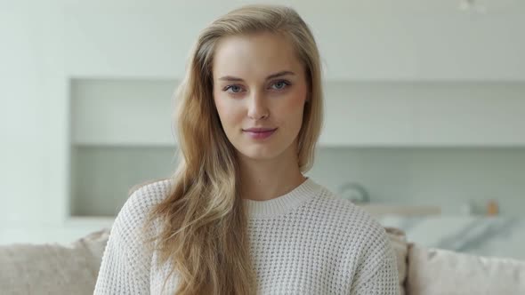 Portrait of a Young Positive Woman with a Healthy Smile Sitting on a Cozy Sofa Looking at the Camera