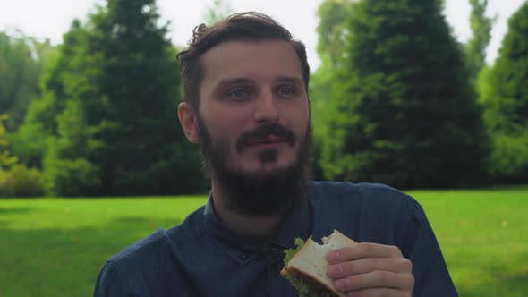 A Young Man Eating a Sandwich with Salad in the Park