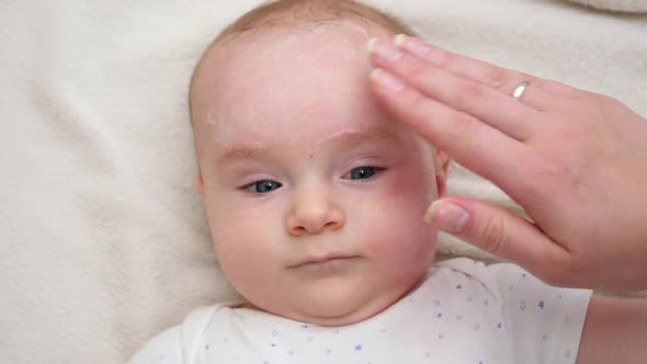 Closeup of Mother Applying Cream for Moisturizing and Cleaning Her Baby's Face