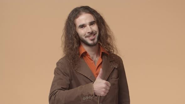 Young Handsome Bearded Man with Long Curly Natural Hair Wearing Brown Hipster Blazer Show Thumbup