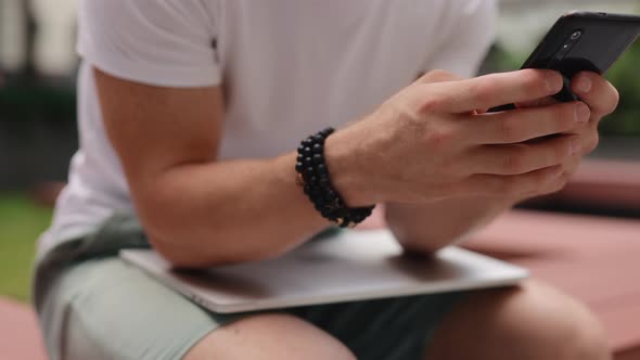 Unrecognizable Man Using Smartphone Sitting at the Yard of Business Center