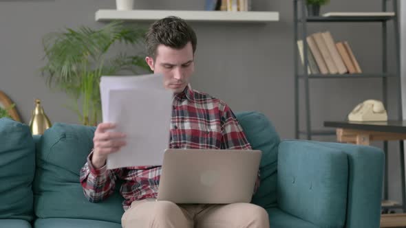 Man with Laptop Reacting to Loss on Documents Sofa