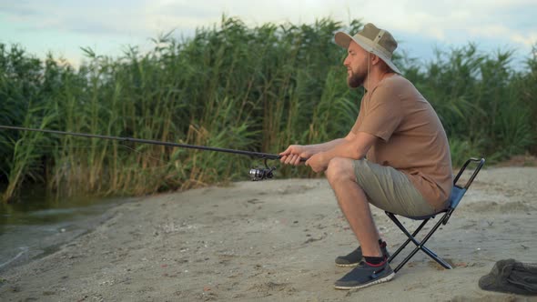 the View From the Back is a Man Fisherman at Dawn on the Lake Catching Fish with a Bait