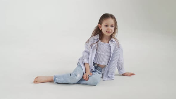 Little Girl with Long Hair in Jeans and Shirt Posing Against a White Background