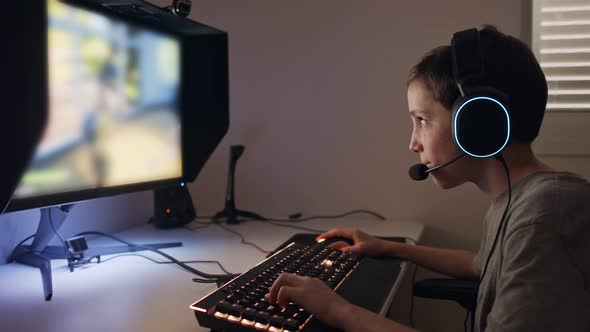 Young boy sitting in front of a computer, playing a game wearing a headset