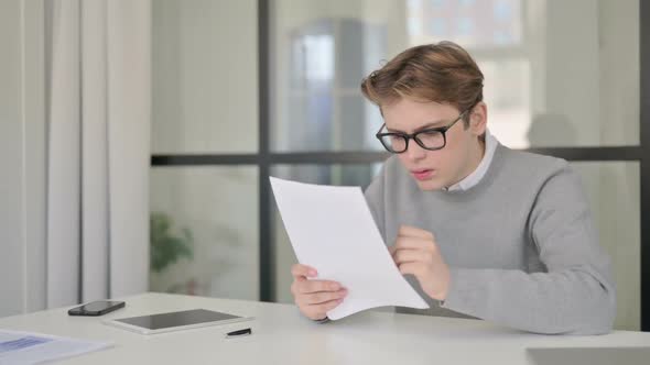 Young Man Feeling Sad While Reading Documents in Modern Office