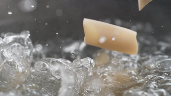 Throwing penne pasta in boiling water. Slow Motion.