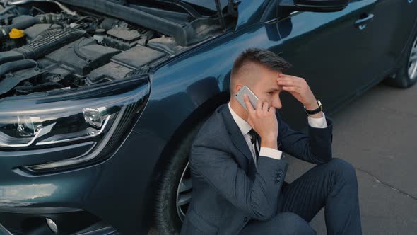 Top View of Sad Young Man Use Smartphone Sitting on Road Near the Broken Car