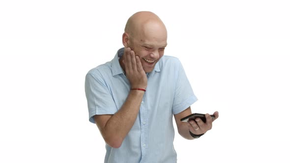 Handsome Adult Bald Guy with Beard Watching Funny Video in Internet Holding Smartphone and Laughing