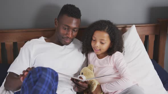 African american father reading a story to his daughter in bed