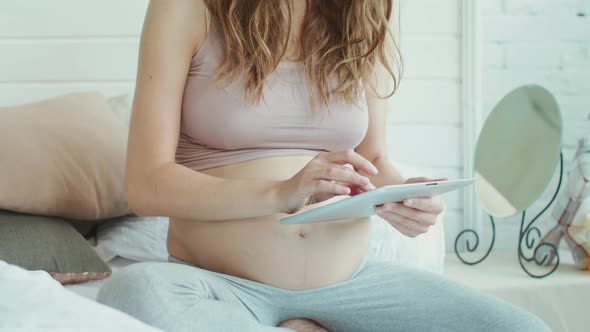 Closeup Unrecignized Belly Mother Serfing on Tablet. Pregnant Woman Relaxing