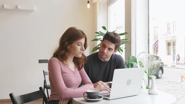 Two Young People Working with a Laptop in a Cafe and Drinking Coffee Slow Motion