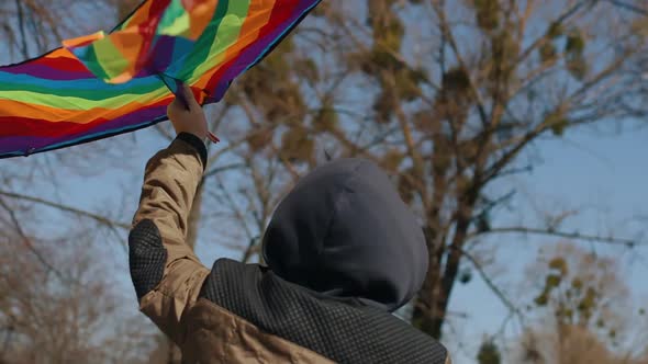 A Happy Boy with a Flying Rainbow Kite Rides a Bicycle on the Road