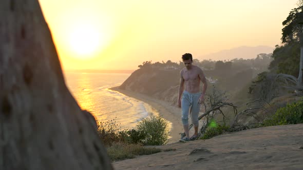 Young fit shirtless man watching a golden sunset after a workout and  run on the edge of a cliff abo