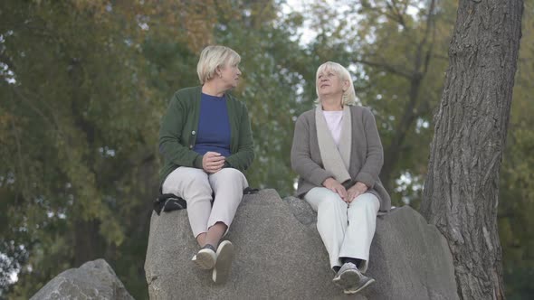 Senior Mother and Her Mature Daughter Sitting on Stones in Park and Talking
