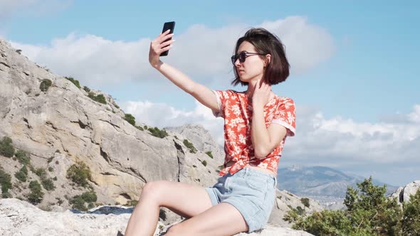 Girl Taking a Selfie on Her Phone Against a Background of Mountains