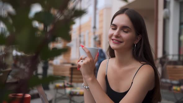 Young attractive girl drinks coffee in a cafe and looks at the camera.