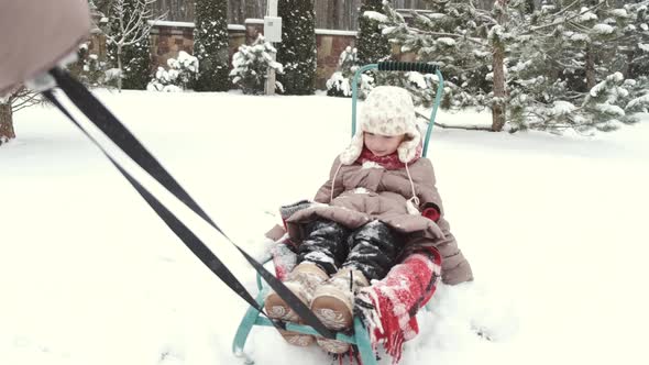 Young Happy Mother and Her Daughter Enjoying a Sledge Ride in a Beautiful Snowy Backyard