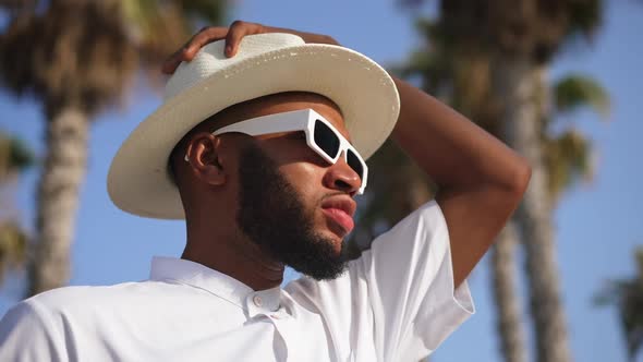 Closeup Portrait of Young Handsome African American Man in Sunglasses Putting on Hat in Slow Motion